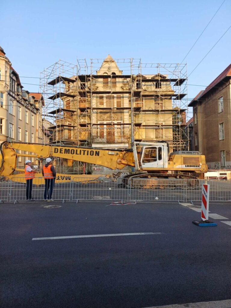 Pierwszy rzut na rozbiórkę kamienicy przy ul. Roosevelta 8 w Poznaniu. Przed budynkiem stoi koparka z napisem Demolition (ang. Rozbiórka)